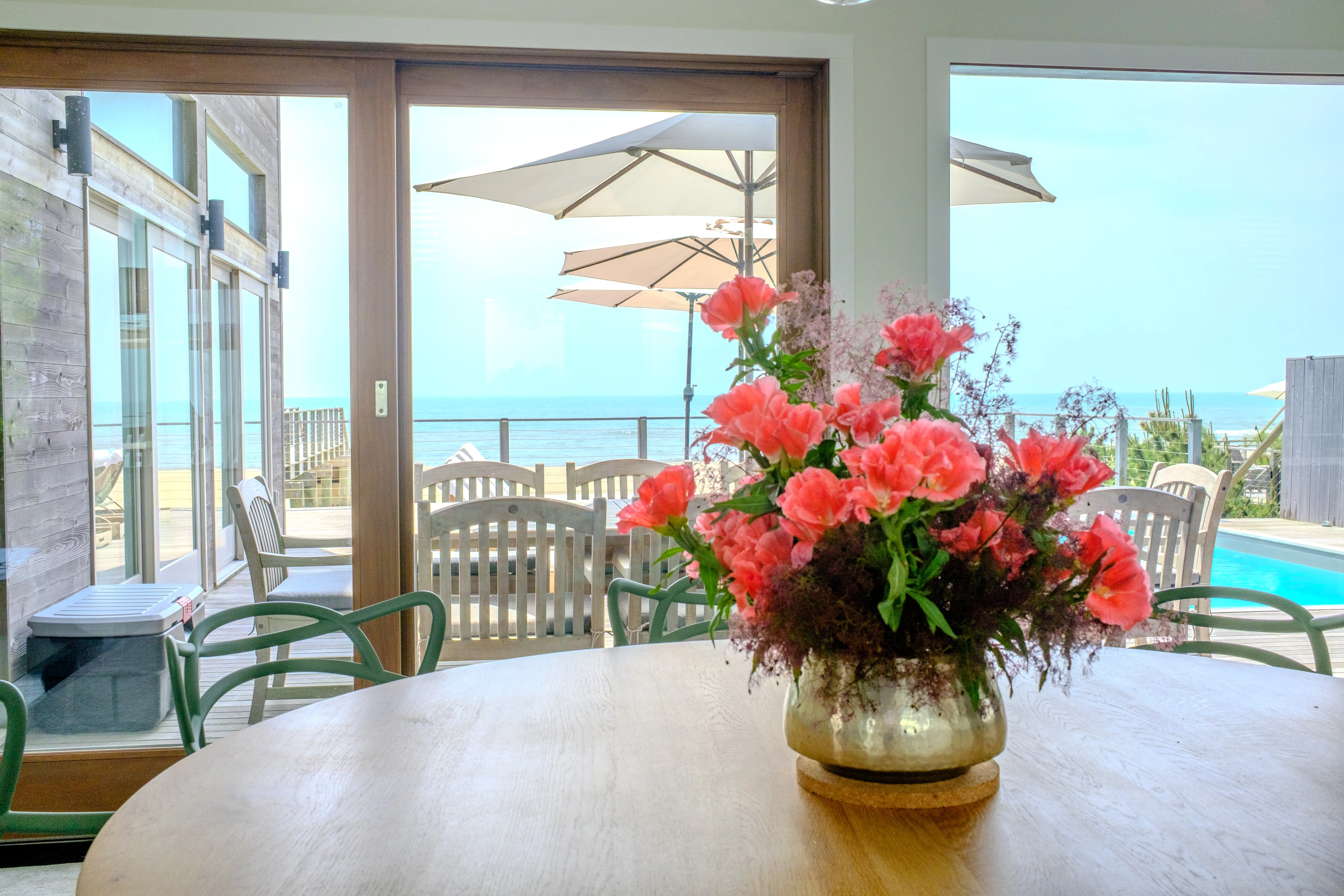 Dining room with a pink floral centerpiece opening onto a pool deck and ocean view.