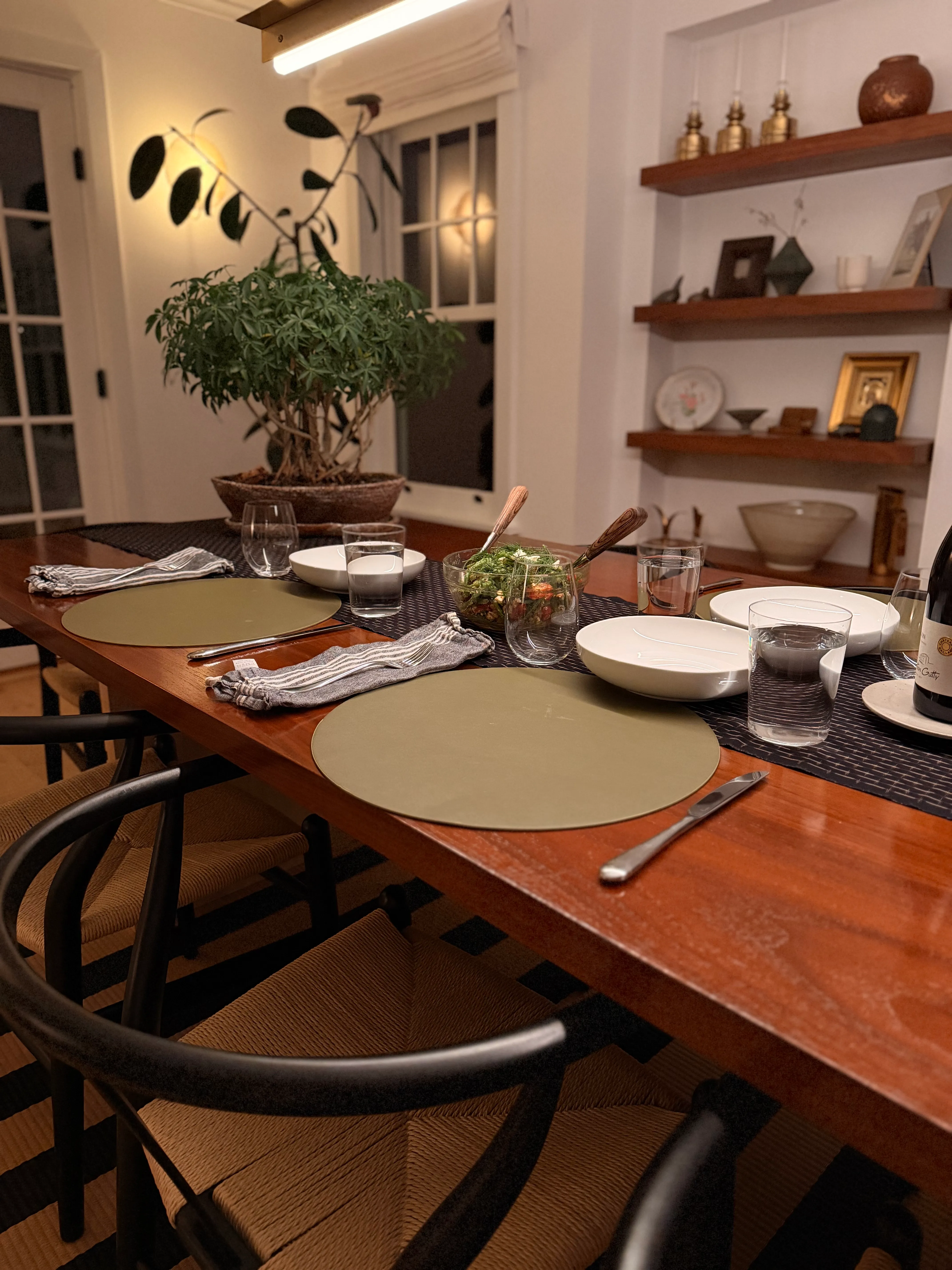 A dining table set with green linen placemats, a fresh salad, and wine — ready for an arrival.