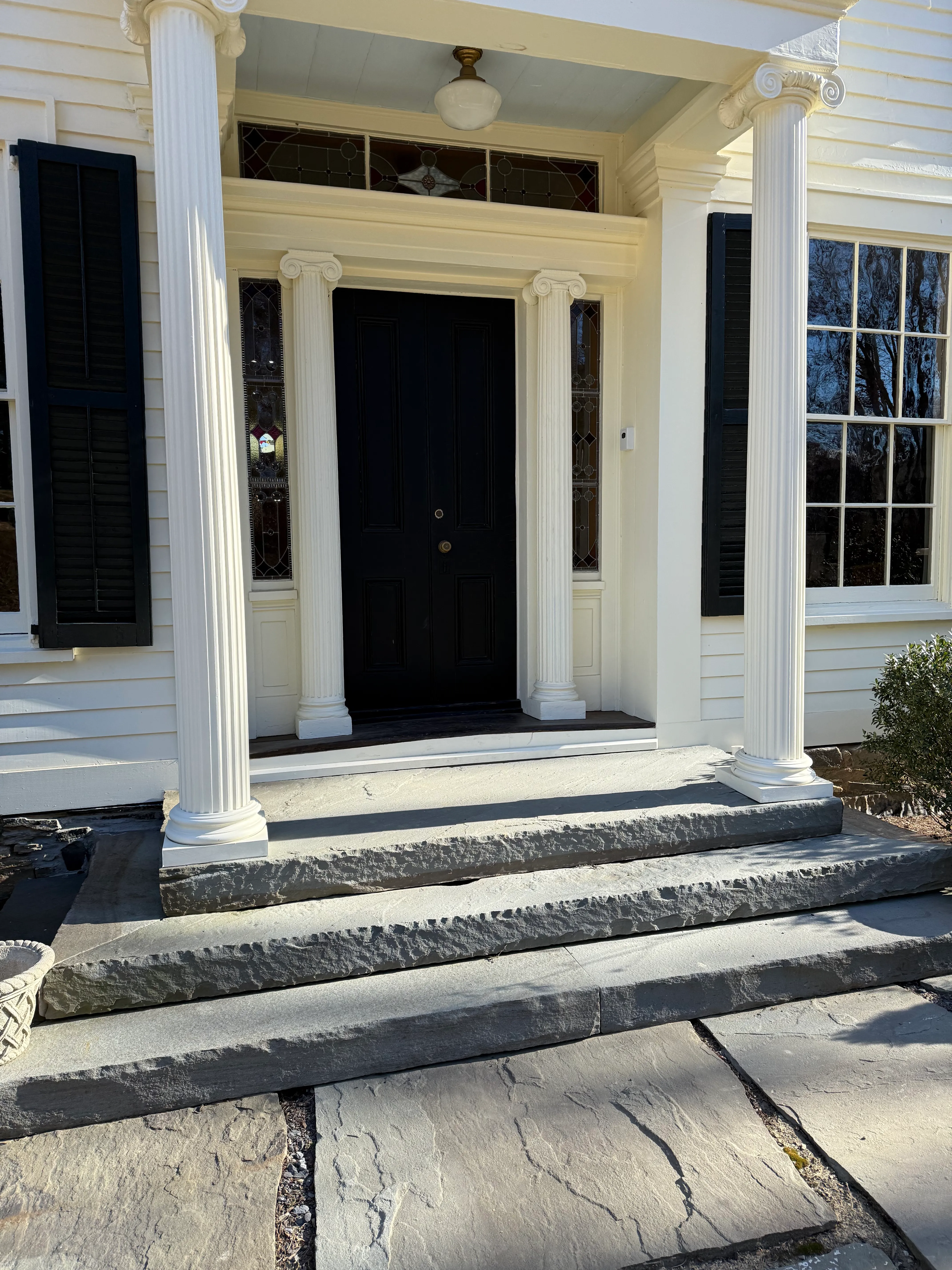 The 1840s Hudson Valley estate: white-painted entrance portico with columns and a black double door.